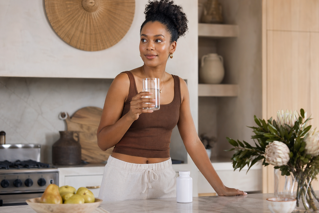 South African woman in a bright modern kitchen taking her daily multivitamin with water