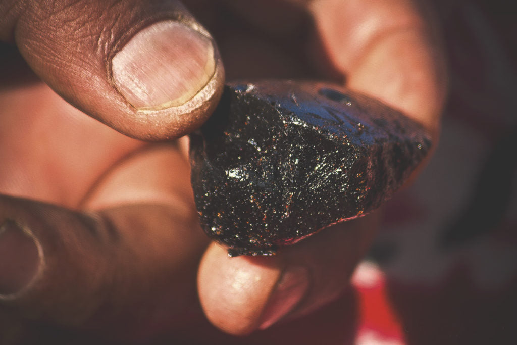 Dark resinous shilajit substance on a wooden spoon with Himalayan rock backdrop